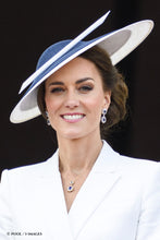 Load image into Gallery viewer, Princess of Wales in a white blazer wearing a wide-brimmed navy and white hat, matching navy earrings, and a blue gemstone necklace